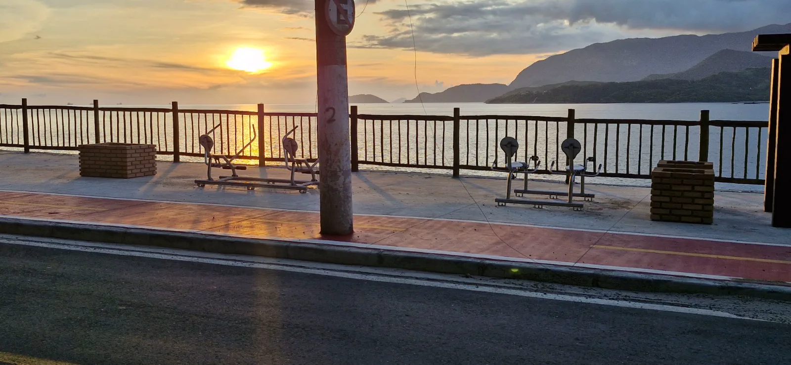 Equipamentos de exercício na orla com o sol se pondo sobre o mar