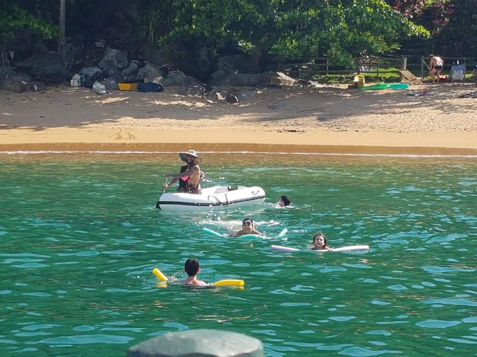 Pessoas nadando em águas verdes diante de uma praia de Ilhabela