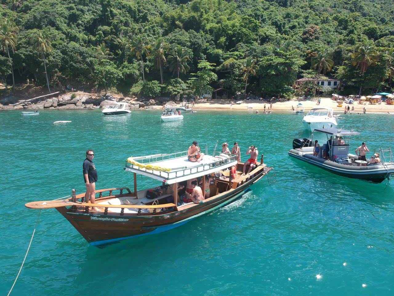 Barco Vibração Positiva ancorado diante de uma praia cercada pela Mata Atlântica